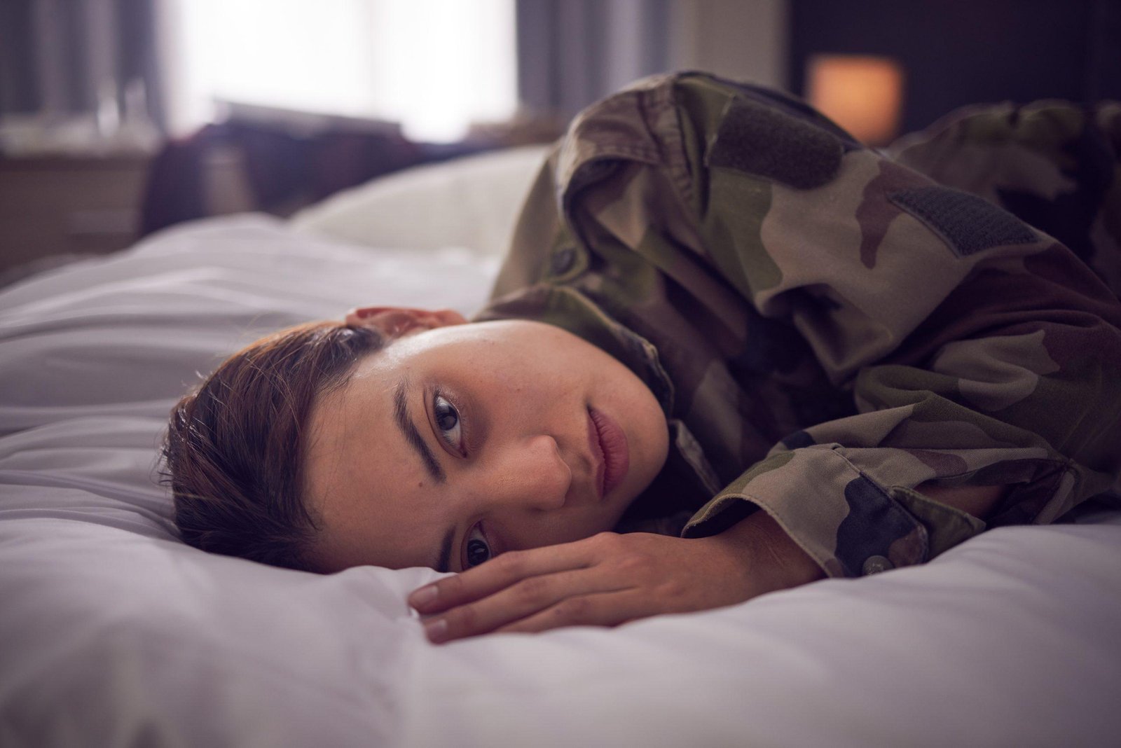 Woman, stress and depression lying on bed in military suffering from Dysthymia Disorder.