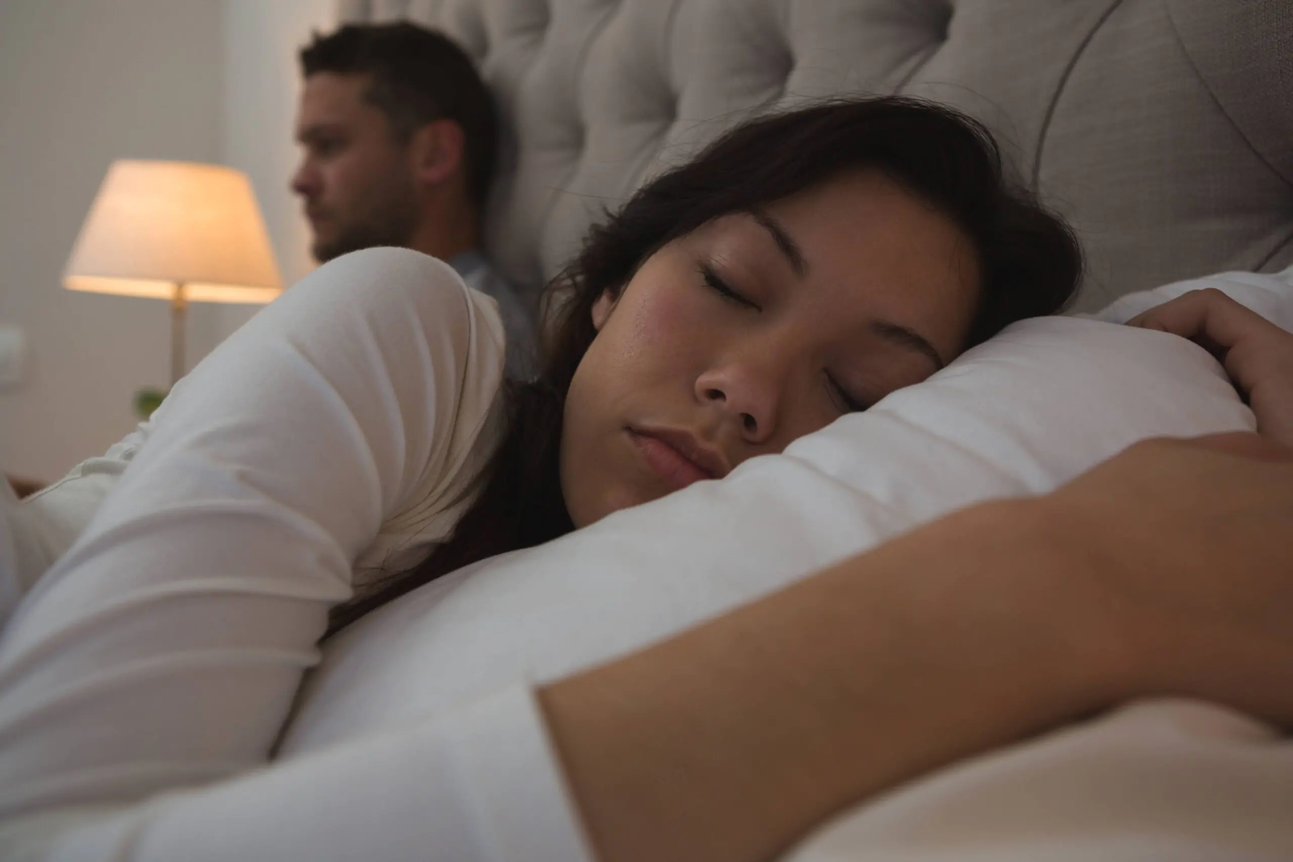 The Impact of Sleep on Mental Health: Contrasting states of rest and wakefulness. A peaceful woman sleeping soundly while her partner remains awake, highlighting the importance of improving sleep quality for nurturing mental well-being.