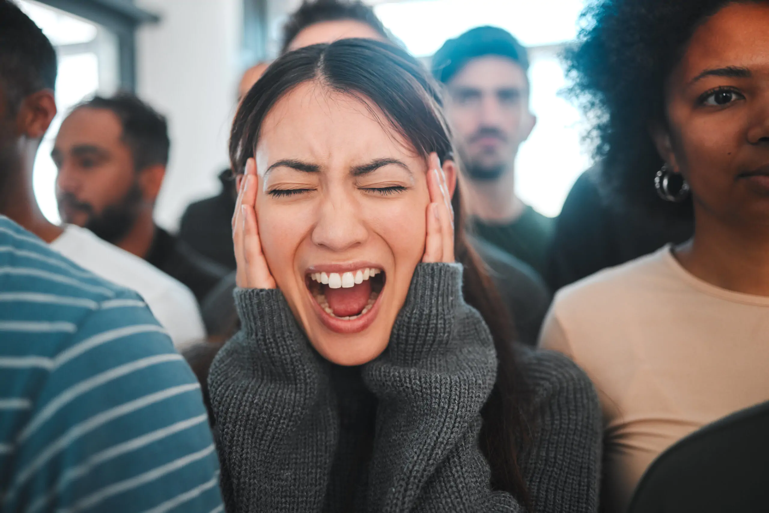 East Coast Telepsychiatry - Panic Disorder Screaming Shot of a young woman experiencing mental illness while being surrounded by people inside.